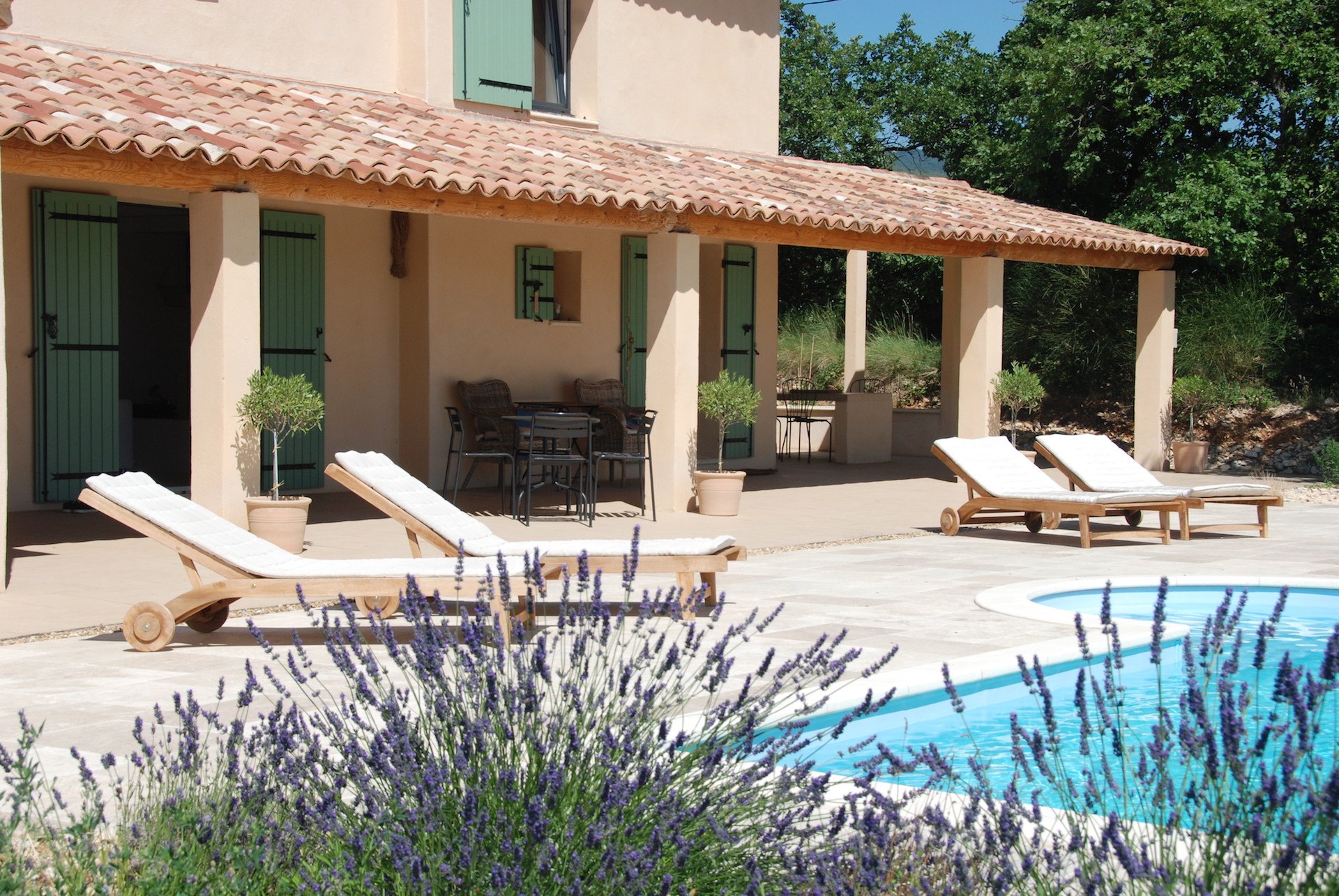 La terrasse couverte, les transats et la piscine derrière la lavande
